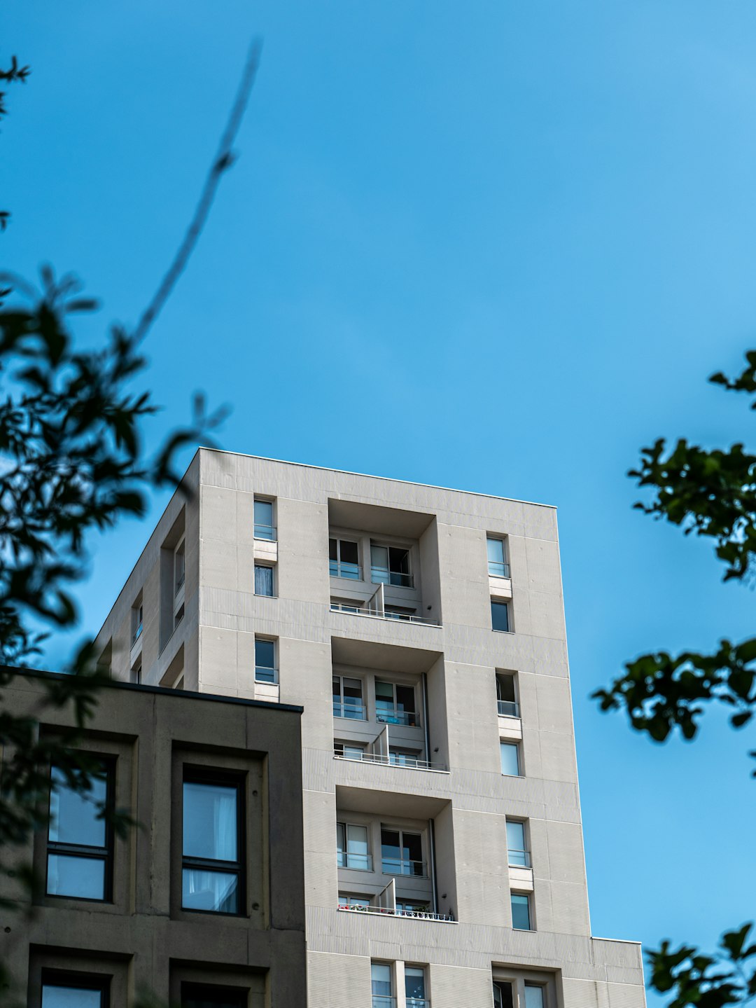 A modern building in the city of Nantes, captured in a low-angle shot. Reflections of the sky and clouds on the building can be seen. Blue and cloudy sky in the background. Sunny.